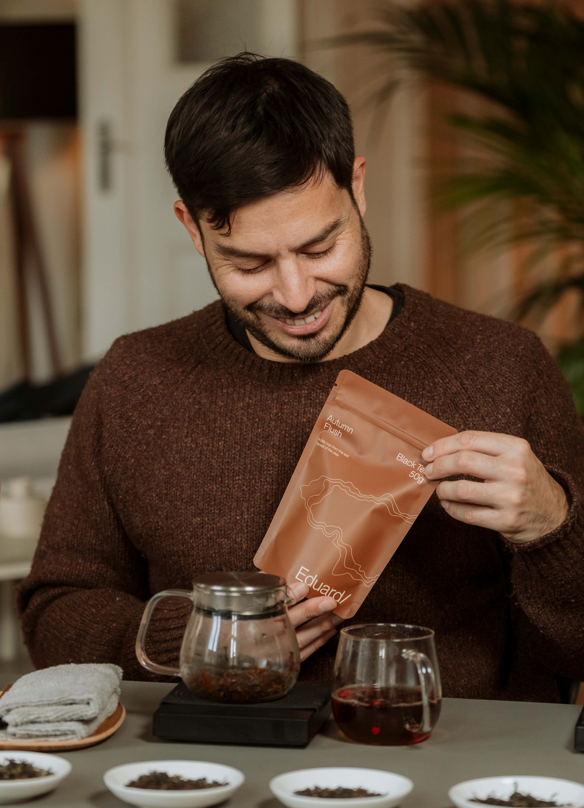 Eduardo opening a pouch of tea at a tasting table with a glass teapot