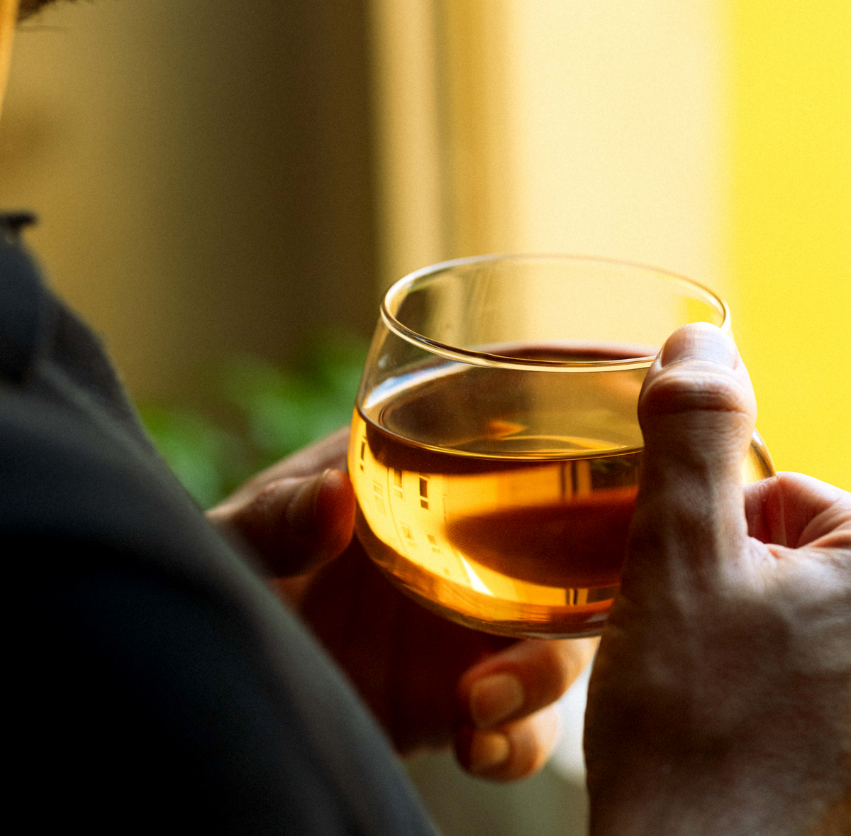 Eine Hand hält ein Glas bernsteinfarbenen Tee